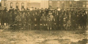Black and white group photo of business men standing on the dirt road of Main Street