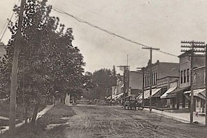 Black and white photo of downtown Oregon. It is a dirt street with electric poles connecting to the buildings