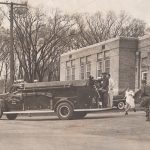 black and white photo of men running to a fire truck outside village hall. This photo was taken in the 1940s